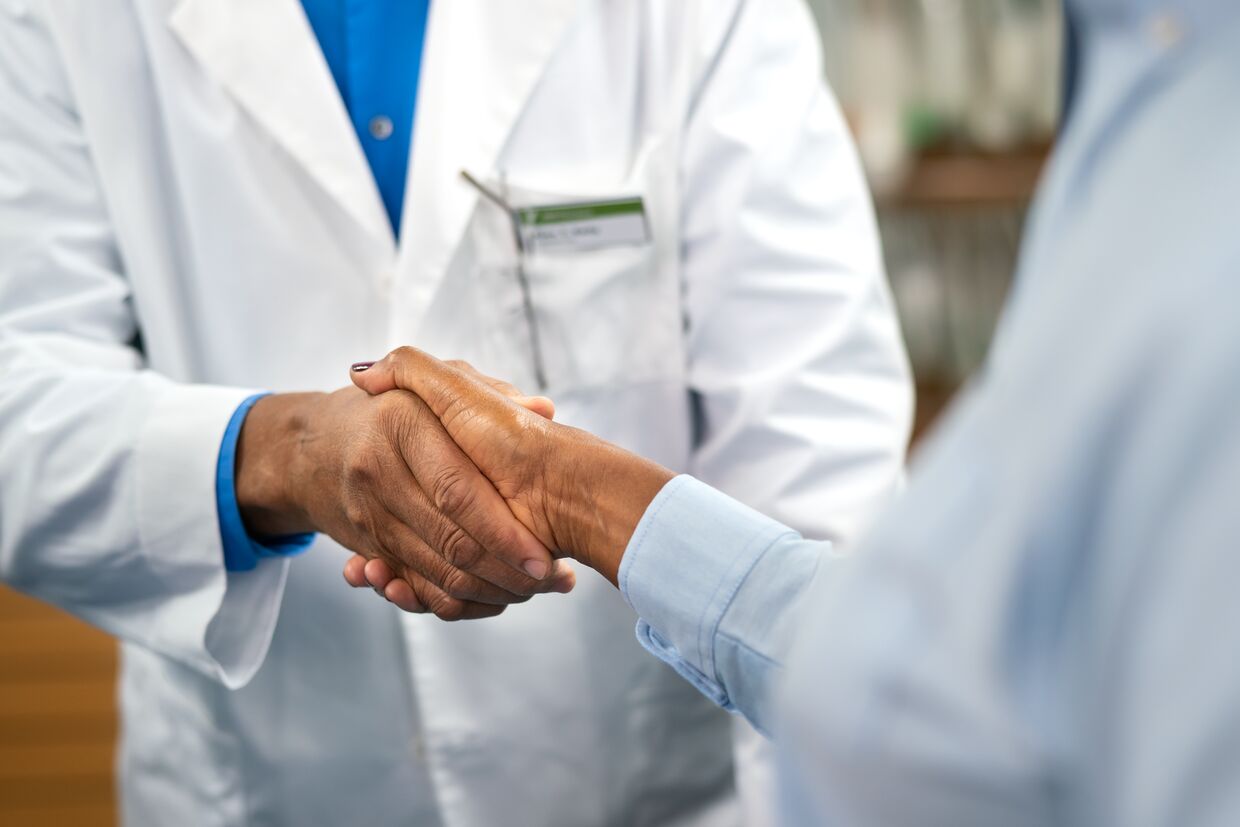 A doctor in a white coat shakes hands with another person, both wearing blue shirts.