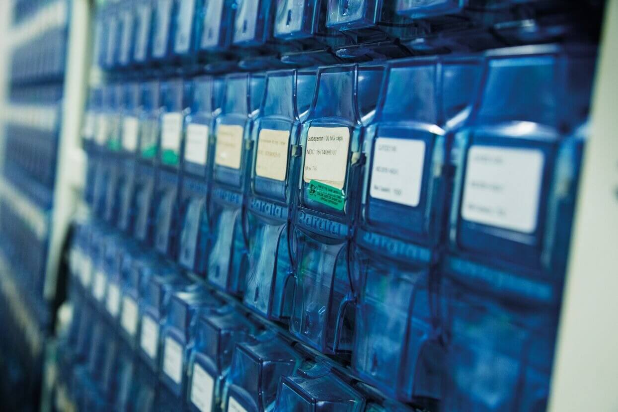 Rows of blue plastic containers with white labels, organized on shelves in a storage system.