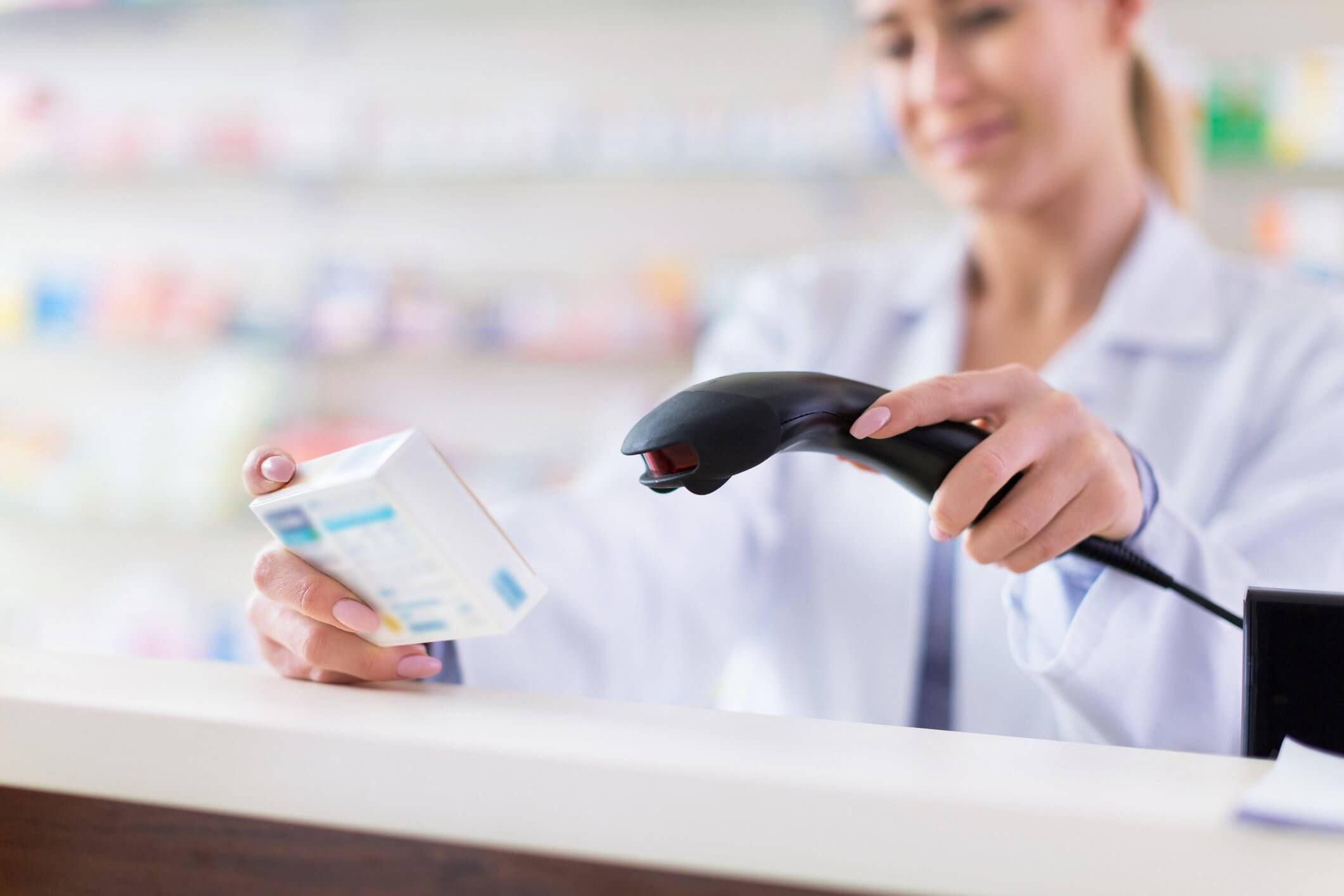 Pharmacist scanning a medication box at a pharmacy counter.