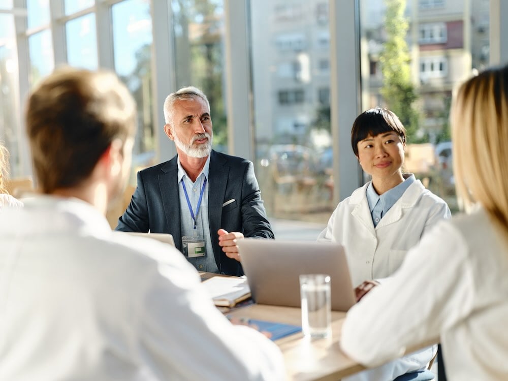 Four people sit around a meeting table with laptops and documents in a conference room.
