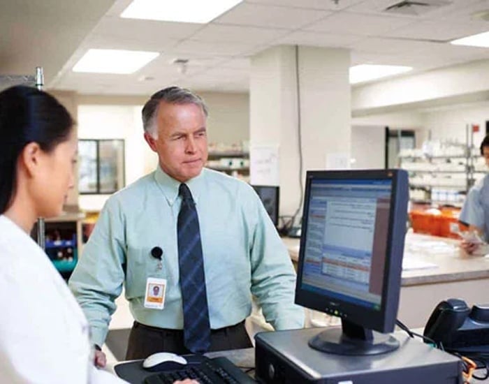 Pharmacy professionals conversing at a computer workstation.
