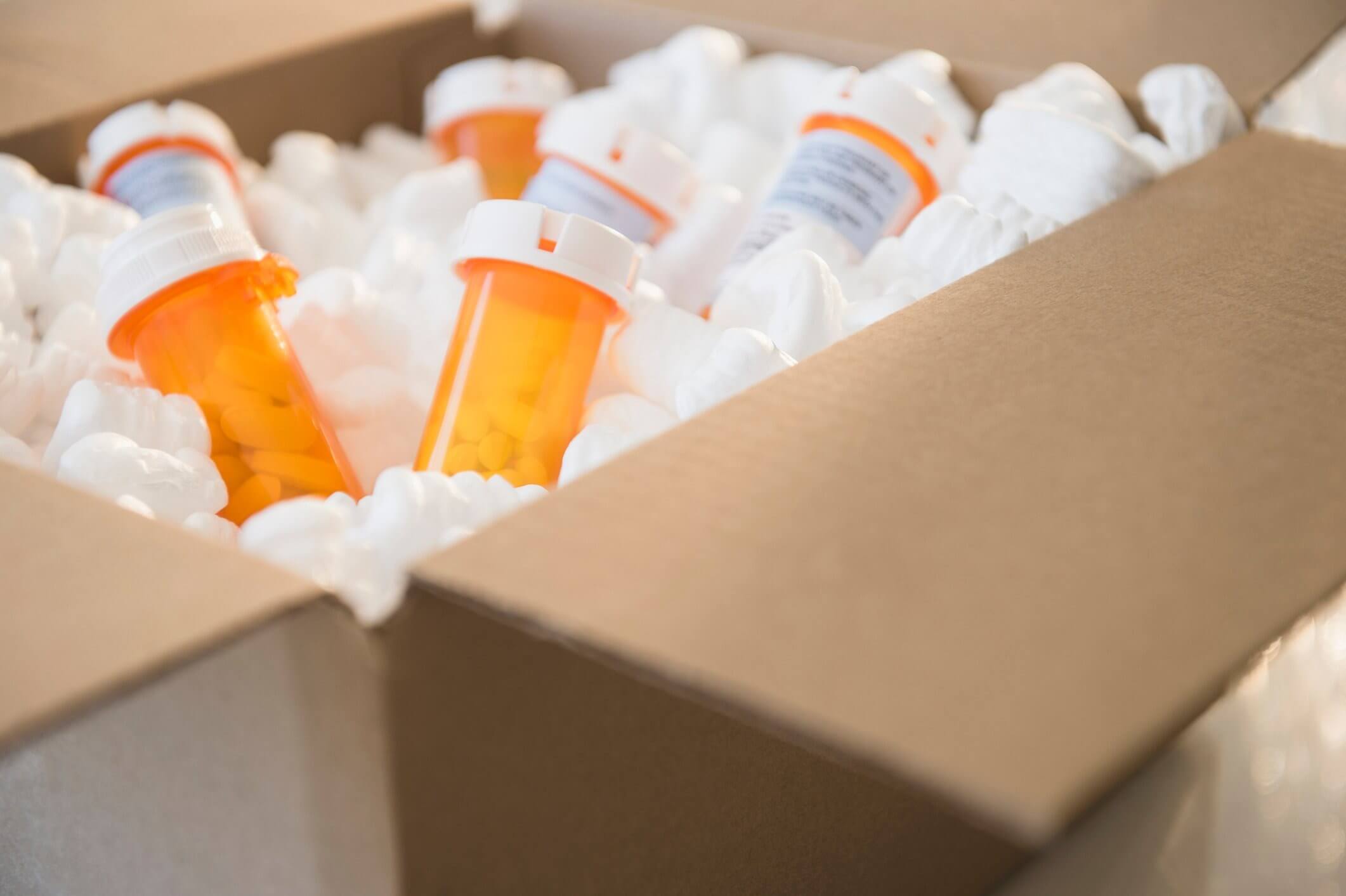 Open cardboard box filled with white packing peanuts and several orange prescription pill bottles.
