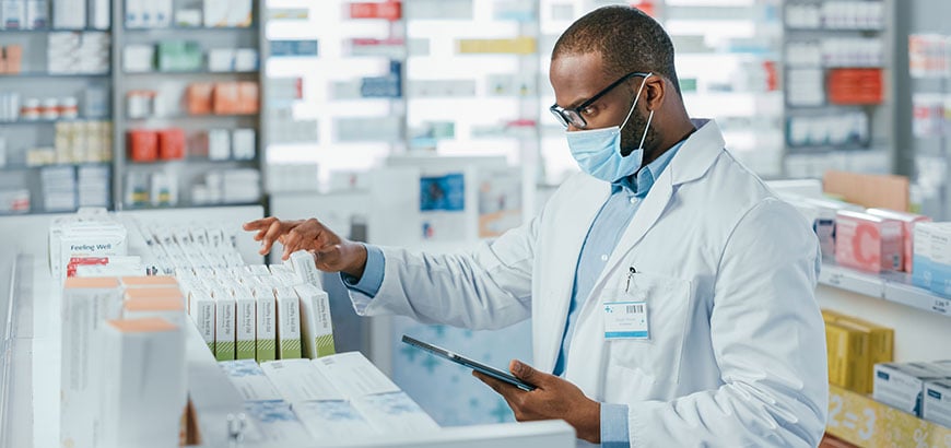 A pharmacist wearing a mask taking inventory of prescription medications