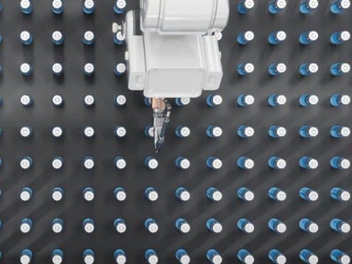 Robotic arms work over a grid of numerous identical bottles on a dark surface.