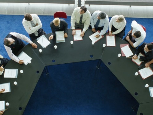 Aerial view of business meeting around a U-shaped table with papers and coffee cups.