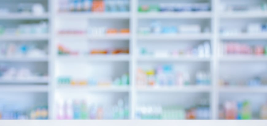 Blurred image of pharmacy shelves filled with assorted medications and healthcare products.