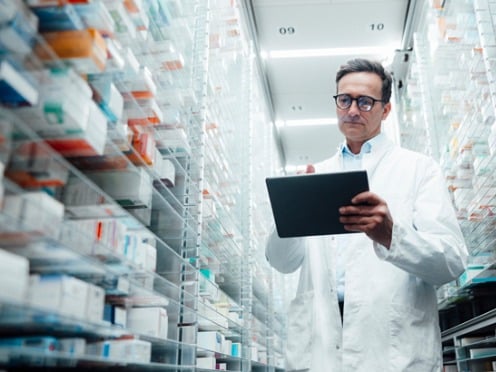 pharmacist with tablet standing in shelves