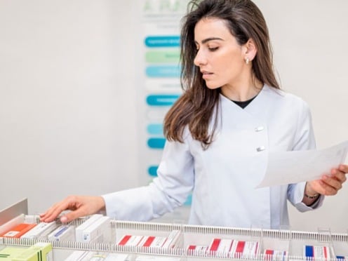 Pharmacist organizing medications in a drawer while holding a sheet of paper.