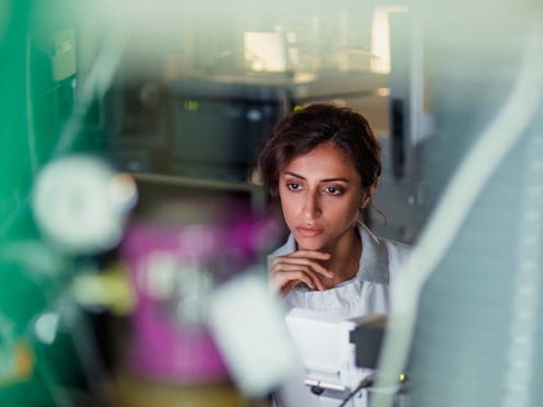 Person seated in a laboratory surrounded by scientific equipment and complex machinery.
