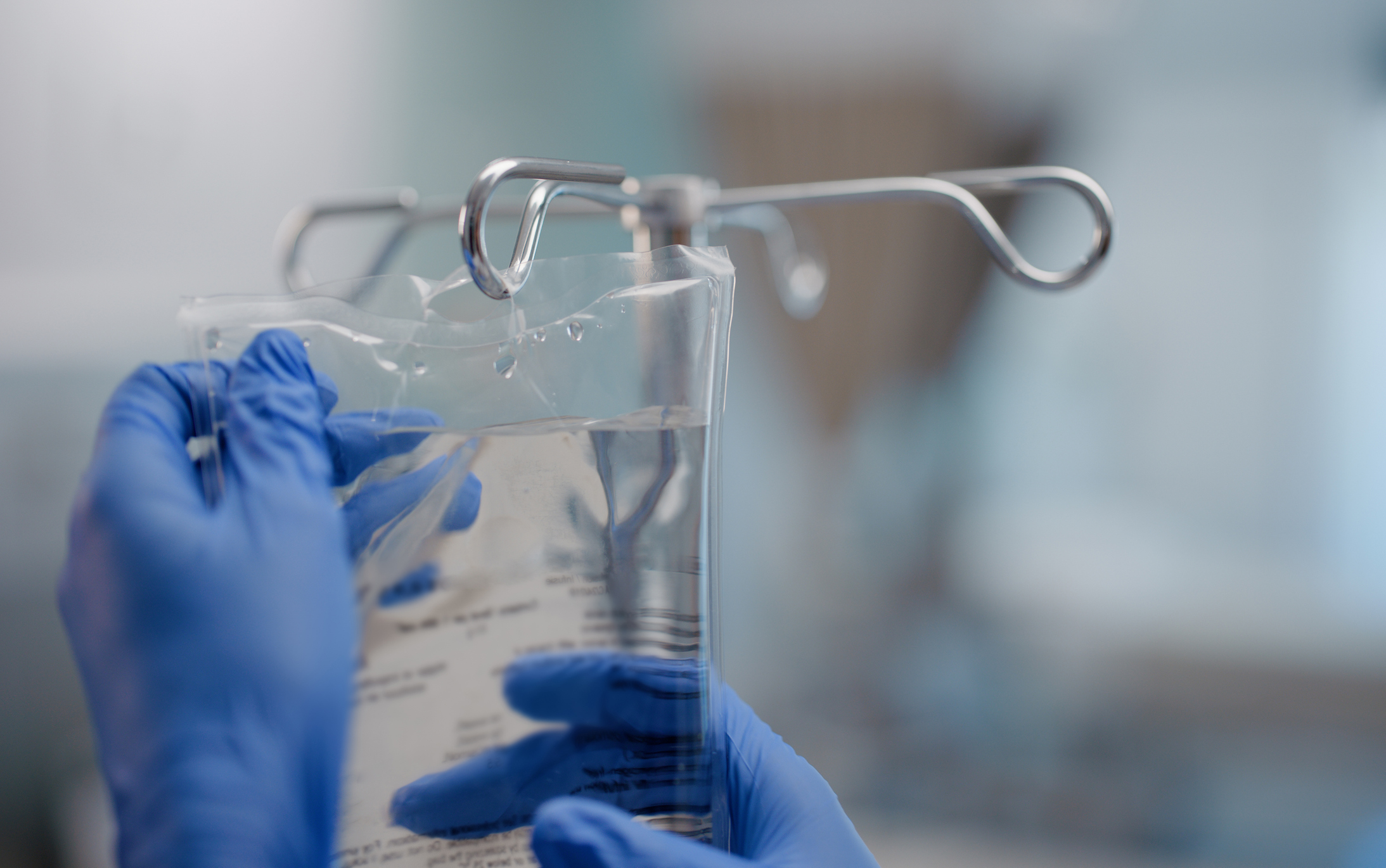 A hand wearing a blue glove puts an IV bag on a hook