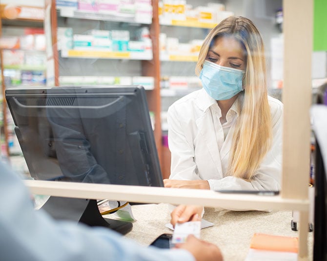 Pharmacist handing an ID card back to a customer over the counter.