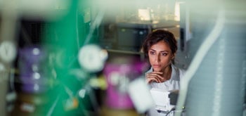 Person in a lab coat partially obscured by laboratory equipment in a clinical setting.