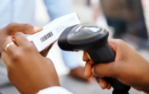 Close-up of a person scanning a barcode on a white box with a handheld barcode scanner.