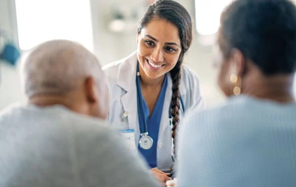 A doctor with a stethoscope talks to two patients in a medical office.