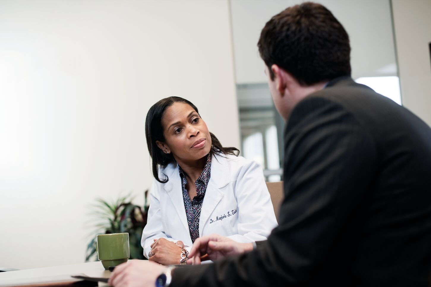 A doctor in a white coat and a man in a suit are having a discussion at a table.