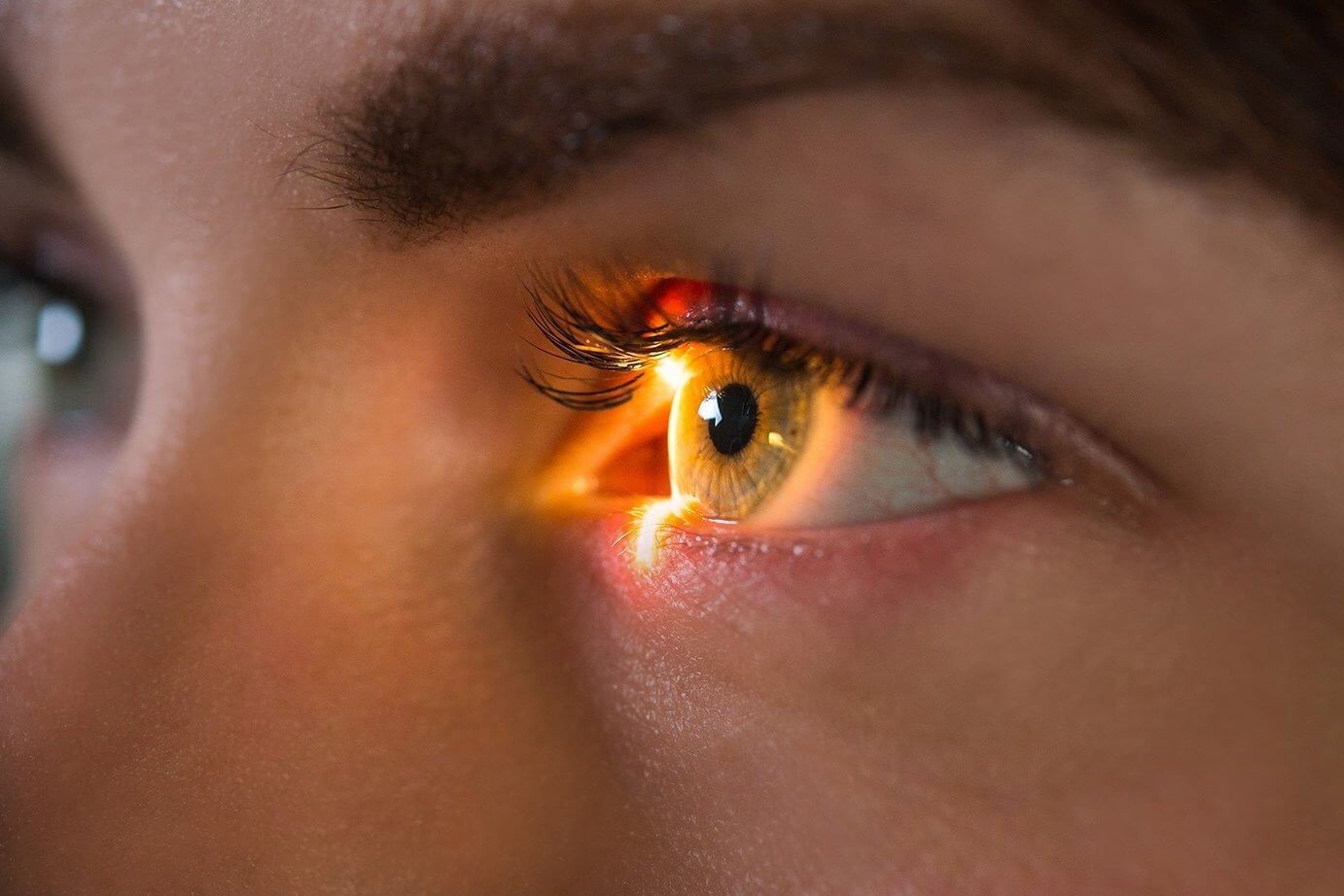 Close-up of a person's eye with a bright light shining into it, highlighting the iris and eyelashes.