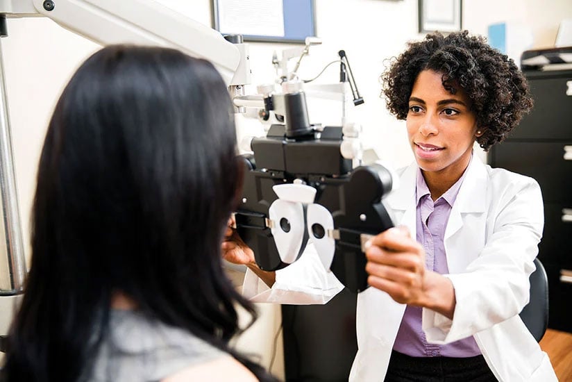 Optometrist performing an eye exam on a patient using a phoropter.