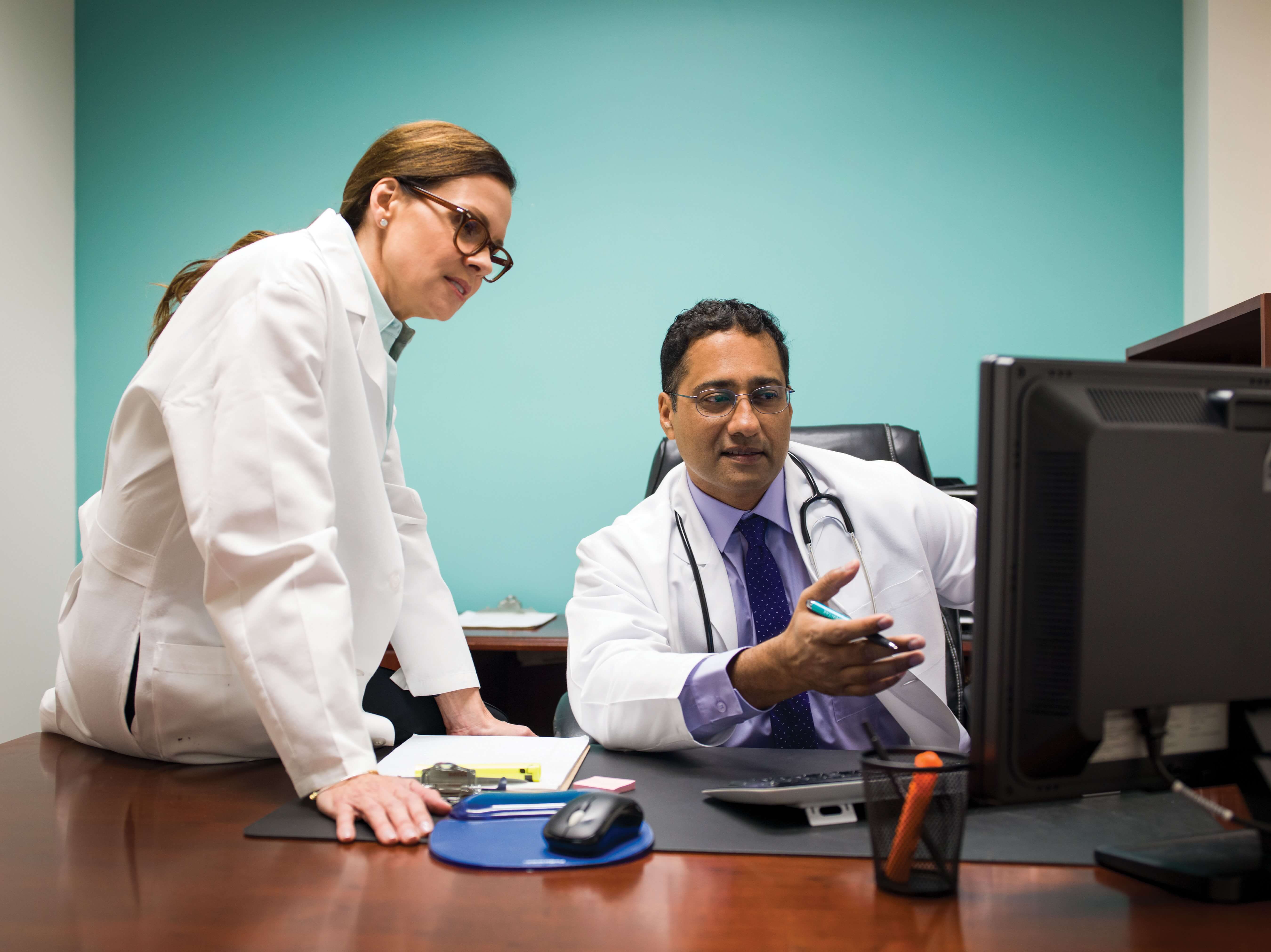 Two doctors in white coats discuss something on a computer screen in a medical office.