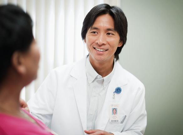 A doctor in a white coat is talking to a patient in a pink shirt.