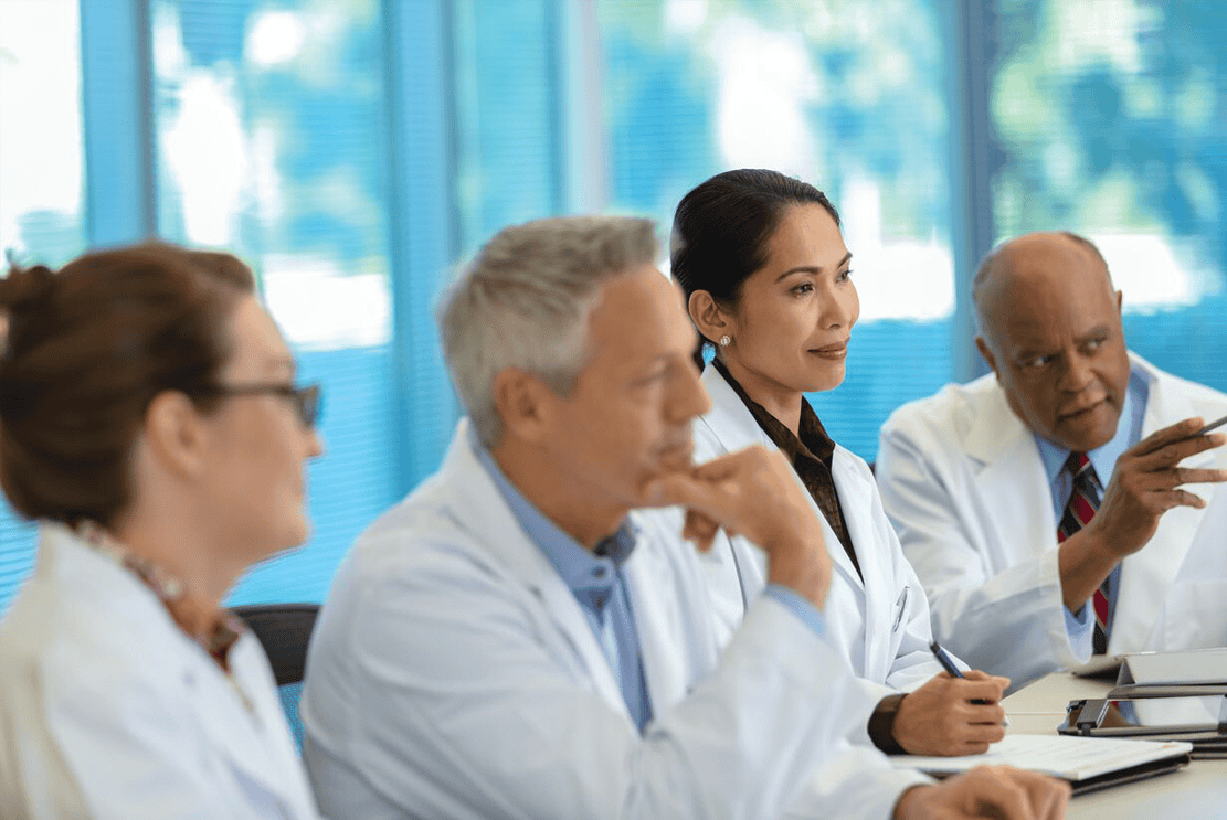 Four people in lab coats sit around a table engaged in discussion