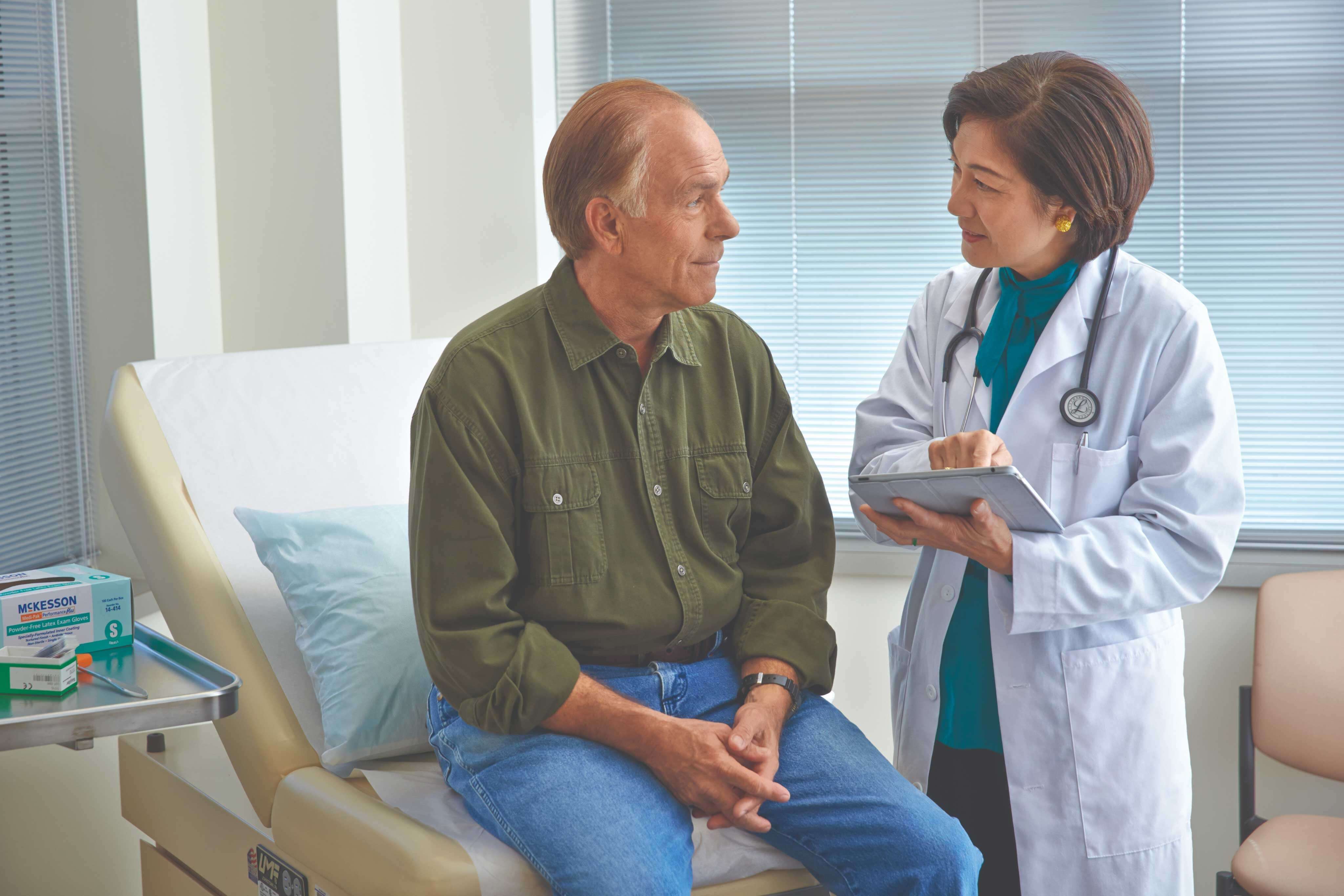 A doctor in a white coat consults with a patient sitting on an examination table.