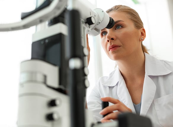 A person in a white lab coat uses an ophthalmic device to examine an eye.