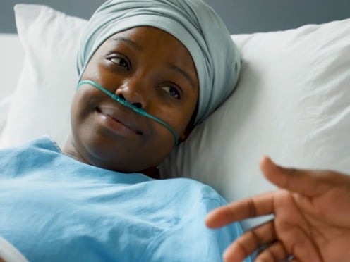 A woman lays in a hospital bed wearing a head wrap and nasal cannula while speaking to a doctor<br>  