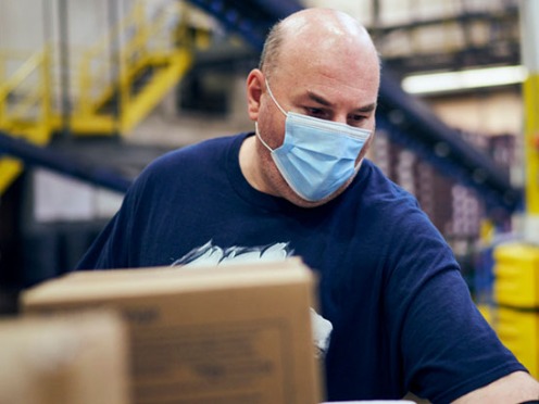 A man with a mask on working inside a distribution center
