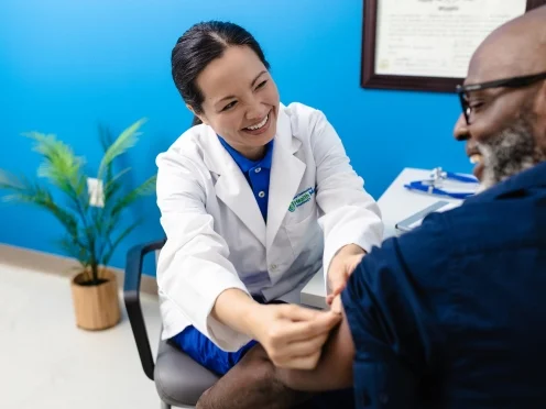 A doctor in a lab coat applies a bandage to a smiling man's arm. 