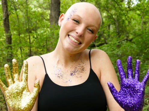 A bald woman shows her hands, one is painted purple and one painted gold.