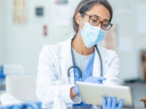 A doctor and a patient wearing masks and looking at a tablet