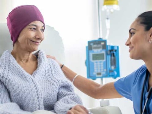 A cancer patient in a hospital bed is comforted by a nurse