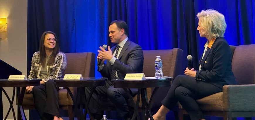 Three people sit on a stage with microphones, participating in a panel discussion.