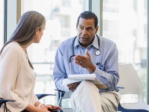 A doctor with a stethoscope is consulting with a seated woman in a bright office.