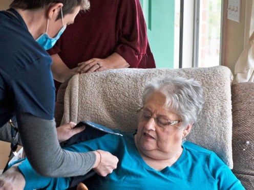 A home nurse checks an elderly patient's blood pressure as she sits in an armchair.