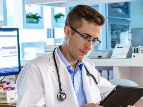 A doctor looking at a tablet standing in front of a computer workstation