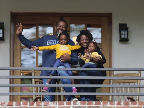 A family standing on a balcony smiling and waving at the camera