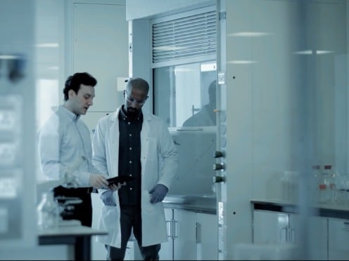 Pharmacist looking at the camera with the title &quot;We'll Be There&quot; over the image.