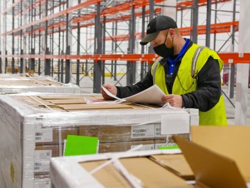 A worker reviewing paperwork while standing in front of a large pallet of boxes
