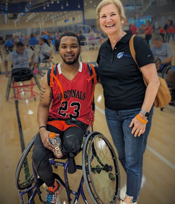 single amputee sitting in wheelchair with woman standing next to him with arms around each other smiling
