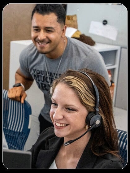 Two coworkers smile while one is wearing a telephone headset