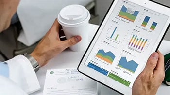 view of persons hands left hand holding to go coffee  right hand holding tablet with charts on it