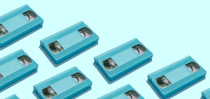 Multiple blue VHS tapes arranged in a diagonal pattern on a light blue background.